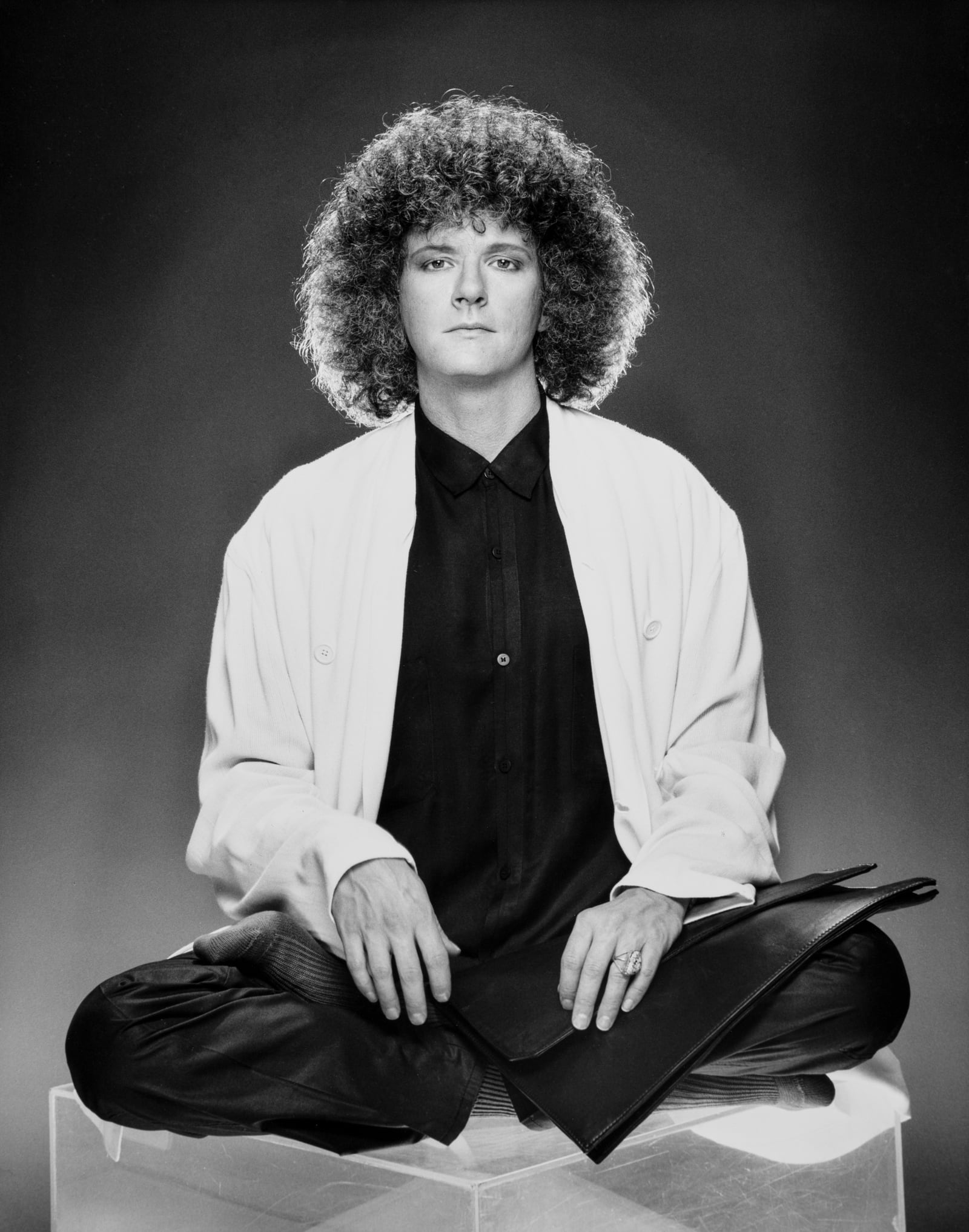 Rama seated in lotus position on a white cube, wearing a white jacket over a black shirt, black and white