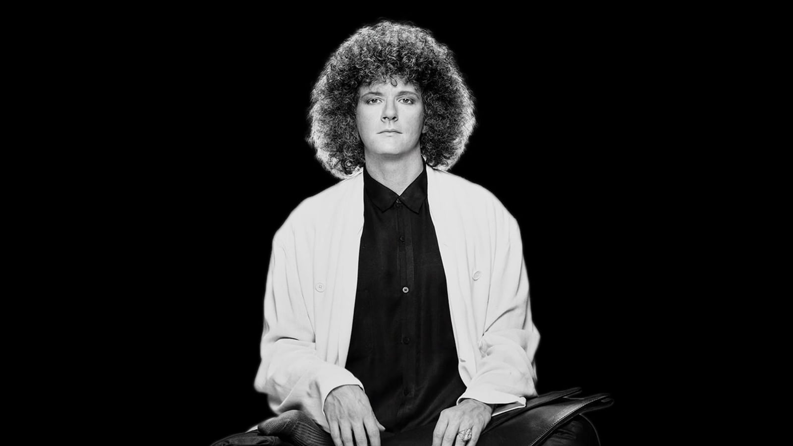 Rama seated in a white jacket over a black shirt, black and white frame from the trailer
